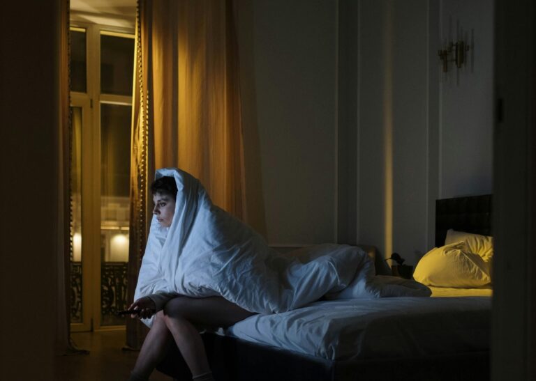 Ágyban ülő nő nyugtalanul próbál elaludni, krónikus fájdalom és alvászavar miatt.